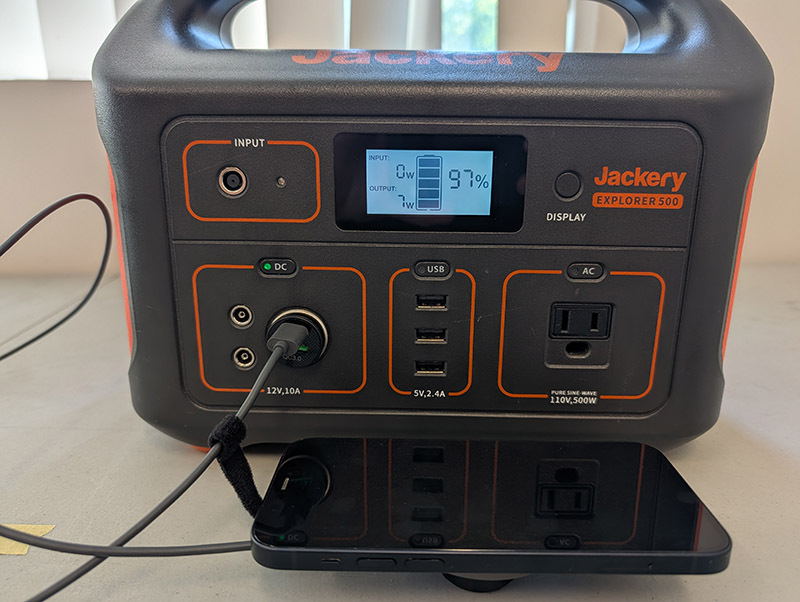 An iPhone charging on a Qi charger connected to the Jackery portable battery.